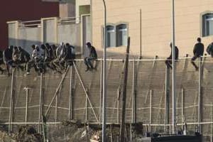 Des migrants assis sur la barrière interdisant l’accès à Melilla. © AFP