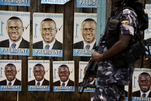 Un policier ougandais monte la garde devant un mur couvert d’affiches à l’effigie de l’opposant Kizza Besigye, à Kampala le 19 février 2016. © Isaac Kasamani/AFP