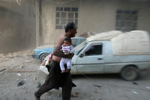 Un homme avec un bébé s’enfuit après des bombardements sur Kafr Batna, dans la banlieue de Damas, le 30 septembre 2016. © AFP