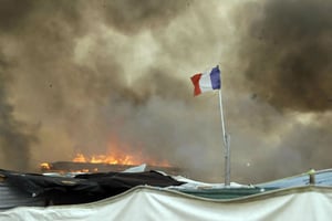 Un drapeau français flotte sur la « jungle » de Calais alors que des baraquements incendiés par des migrants prennent feu, le 26 octobre 2016. © Matt Dunham/AP/SIPA