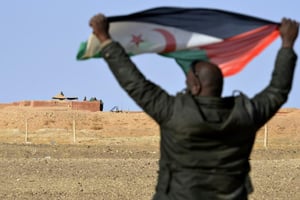 Un sahraoui brandit un drapeau du front polisario, non loin de soldats marocains surveillant le mur de défense au nord-ouest du territoire, près d’El-Mahbes, dans un secteur sous contrôle sahraoui, le 3 février 2017. © Stringer/AFP