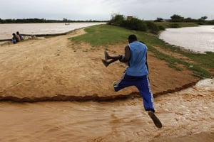 Un homme, son neveu dans les bras, saute un ruisseau qui débordait les rives du fleuve Niger, à Niamey, le vendredi 31 juillet 2009. © Rebecca Blackwell/AFP