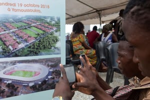 Les gens prennent des photos d’une pancarte représentant un futur stade à Yamoussoukro, le 19 octobre 2018. © AFP.