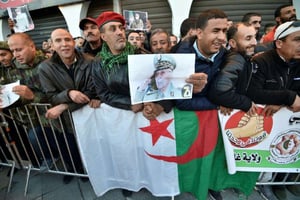 Des Algériens se rassemblent avec le drapeau national et des portraits de l’ancien chef militaire algérien, le général Ahmed Gaïd Salah, devant le Palais du Peuple en prévision de ses funérailles à Alger le 25 décembre 2019. © AFP / Ryad Kramdi