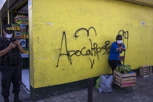 Une femme masquée attend avec ses achats à côté d’une inscription murale « Apocalypse » à Lima, au Pérou, le 19 mars. © Rodrigo Abd/AP/SIPA
