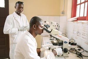 JAD20201118-ASS-Tribune-MoniqueWasunna-Photo2 Leon Katunda and Freddy Luwey, Head of the Laboratory, analyse cerebrospinal fluid under microscopes with the aid of specialized software and a tablet that can take photos. These are used as part of DNDi’s trials and imagery can be sent using an internet connection that DNDi set up at the site.
© Xavier Vahed-DNDI