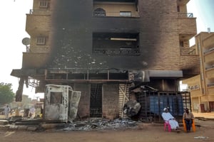 Des hommes sont assis devant une agence bancaire incendiée dans le sud de Khartoum, le 24 mai 2023. © AFP