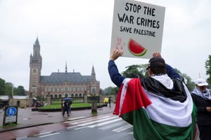 Un manifestant drapé dans un drapeau palestinien brandit une pancarte lors d’une manifestation de soutien aux Palestiniens de Gaza devant la Cour internationale de justice (CIJ), le jour d’une décision sur la demande de l’Afrique du Sud d’ordonner l’arrêt de l’offensive israélienne de Rafah à Gaza © REUTERS/Johanna Geron