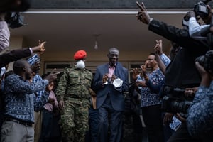 Le vétéran de l’opposition ougandaise Kizza Besigye (au centre) réagit alors que ses partisans et les médias le regardent être escorté par la police militaire hors de la Cour martiale de Makindye à Kampala, le 20 novembre 2024. © Badru Katumba / AFP